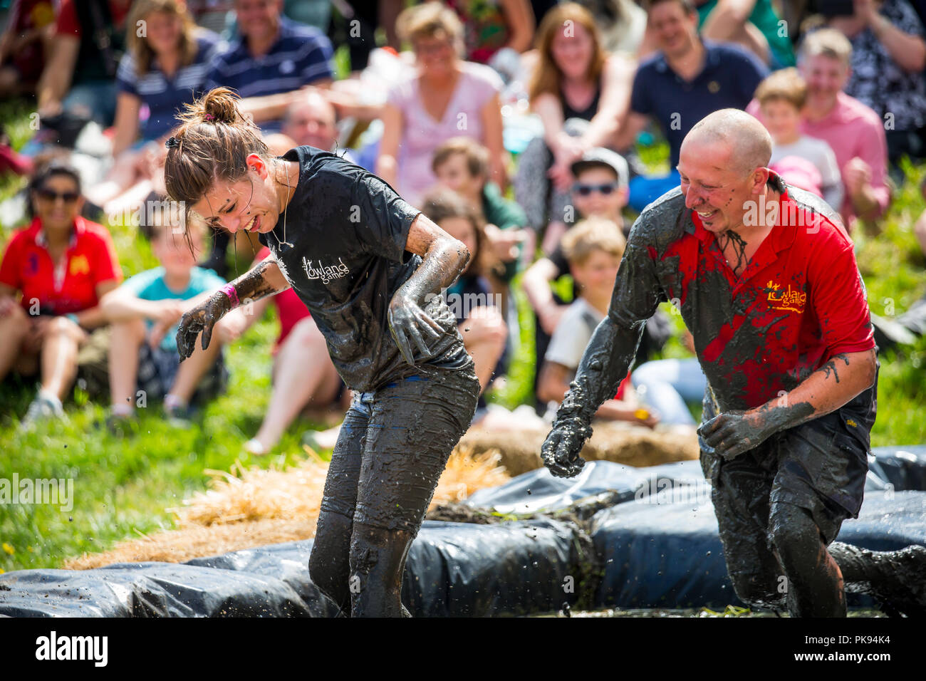 A man in a mud wrestling pit at the Lowland Games  chases a woman to make her more muddy Stock Photo