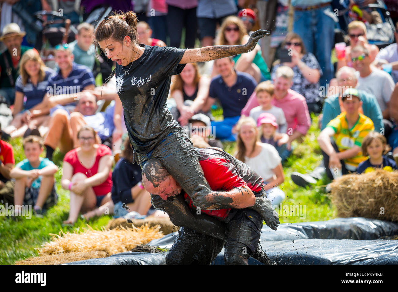 Man carrying a woman over a dirty and wet obstacle course at The Lowland Games in Thorney, Somerset, England Stock Photo