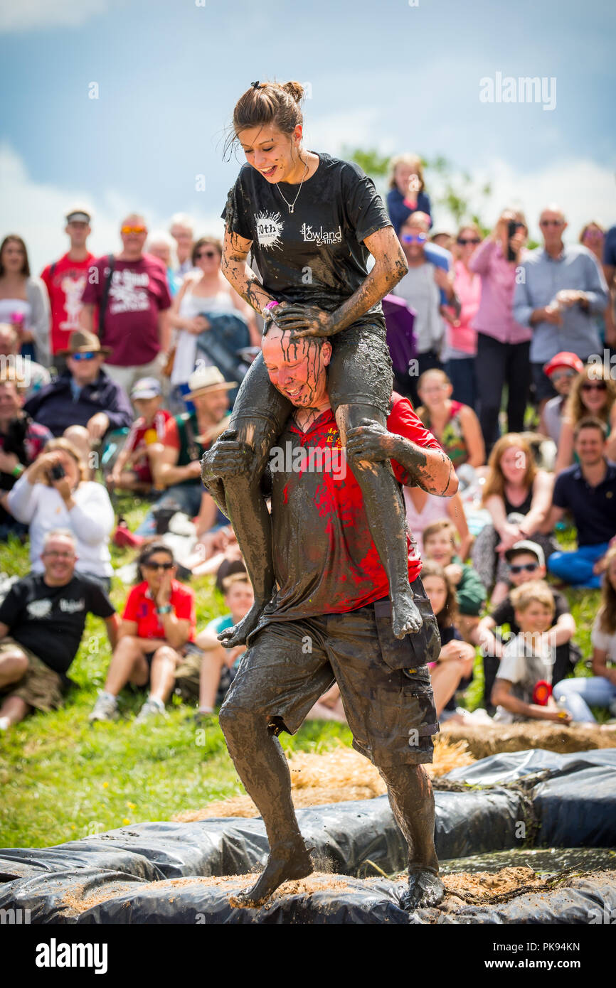 Man carrying a woman over a dirty and wet obstacle course at The Lowland Games in Thorney, Somerset, England Stock Photo