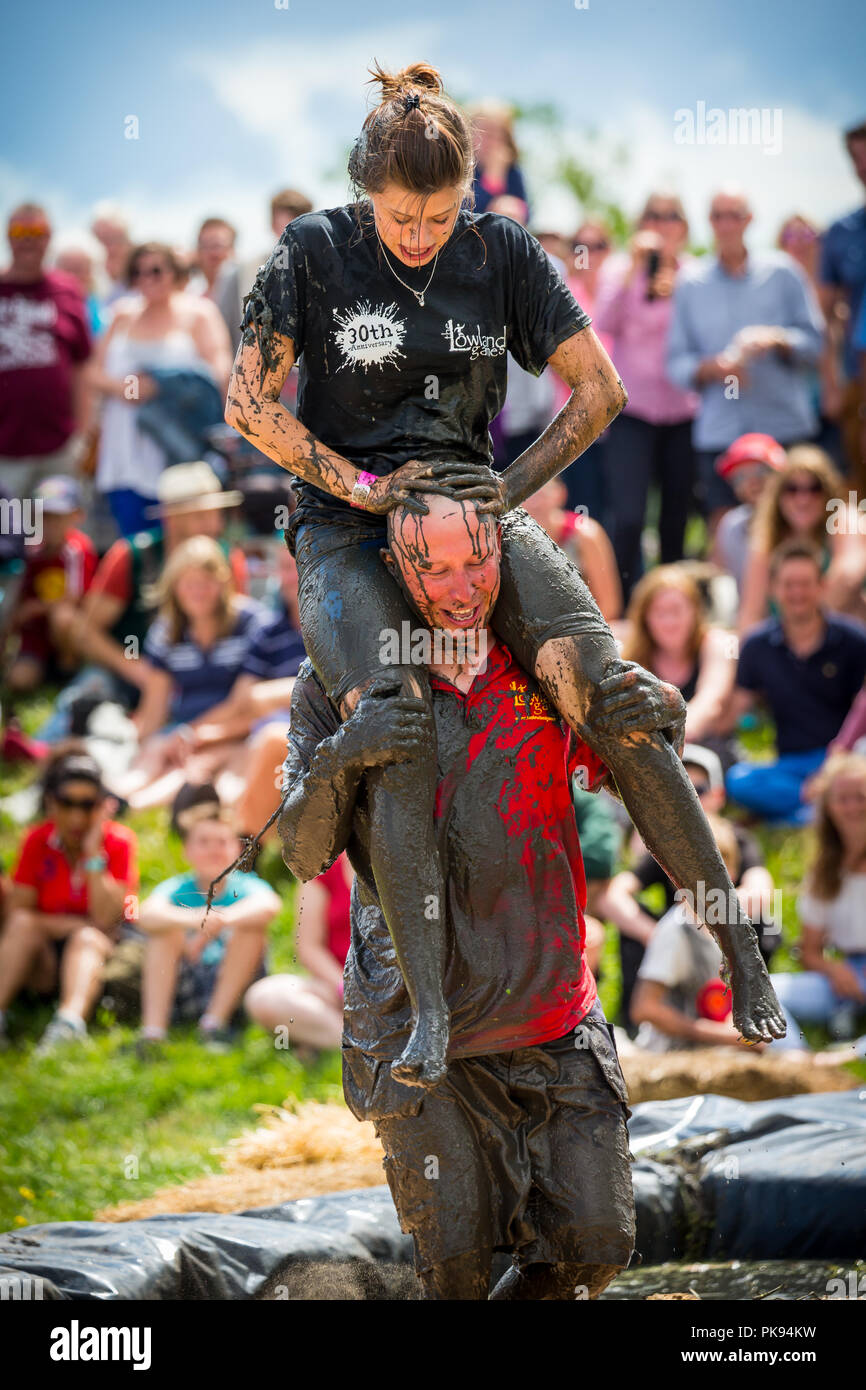 Man carrying a woman over a dirty and wet obstacle course at The Lowland  Games in Thorney, Somerset, England Stock Photo - Alamy