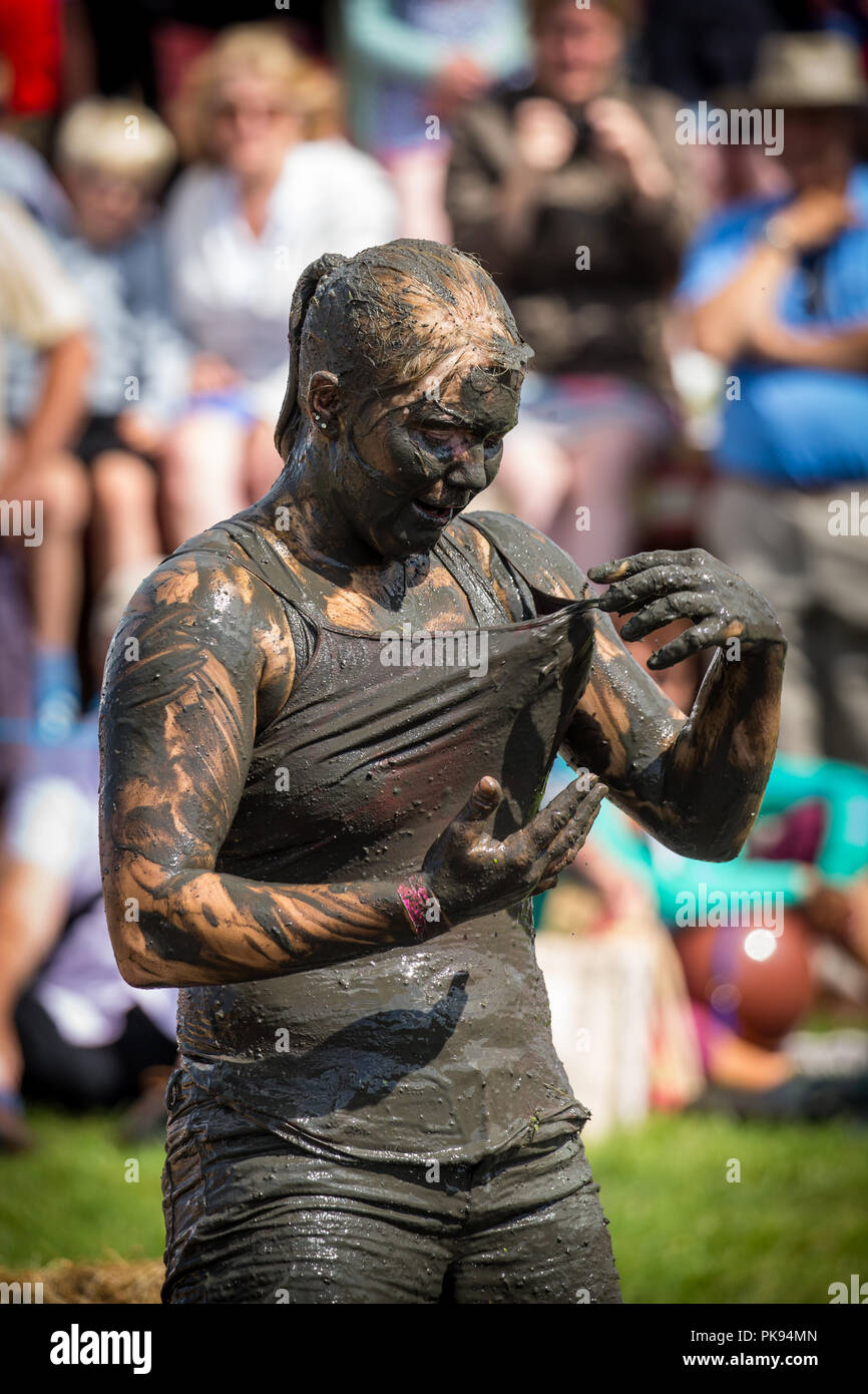 A woman stands covered in mud in the mud wrestling pit at The Lowland Games in Somerset with people watching behind her Stock Photo