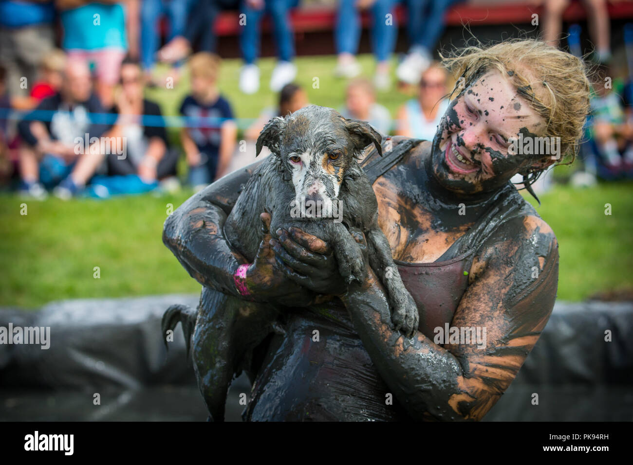 A mud covered woman at the Lowland Games holds her dirty muddy dog in the mud wrestling pit Stock Photo