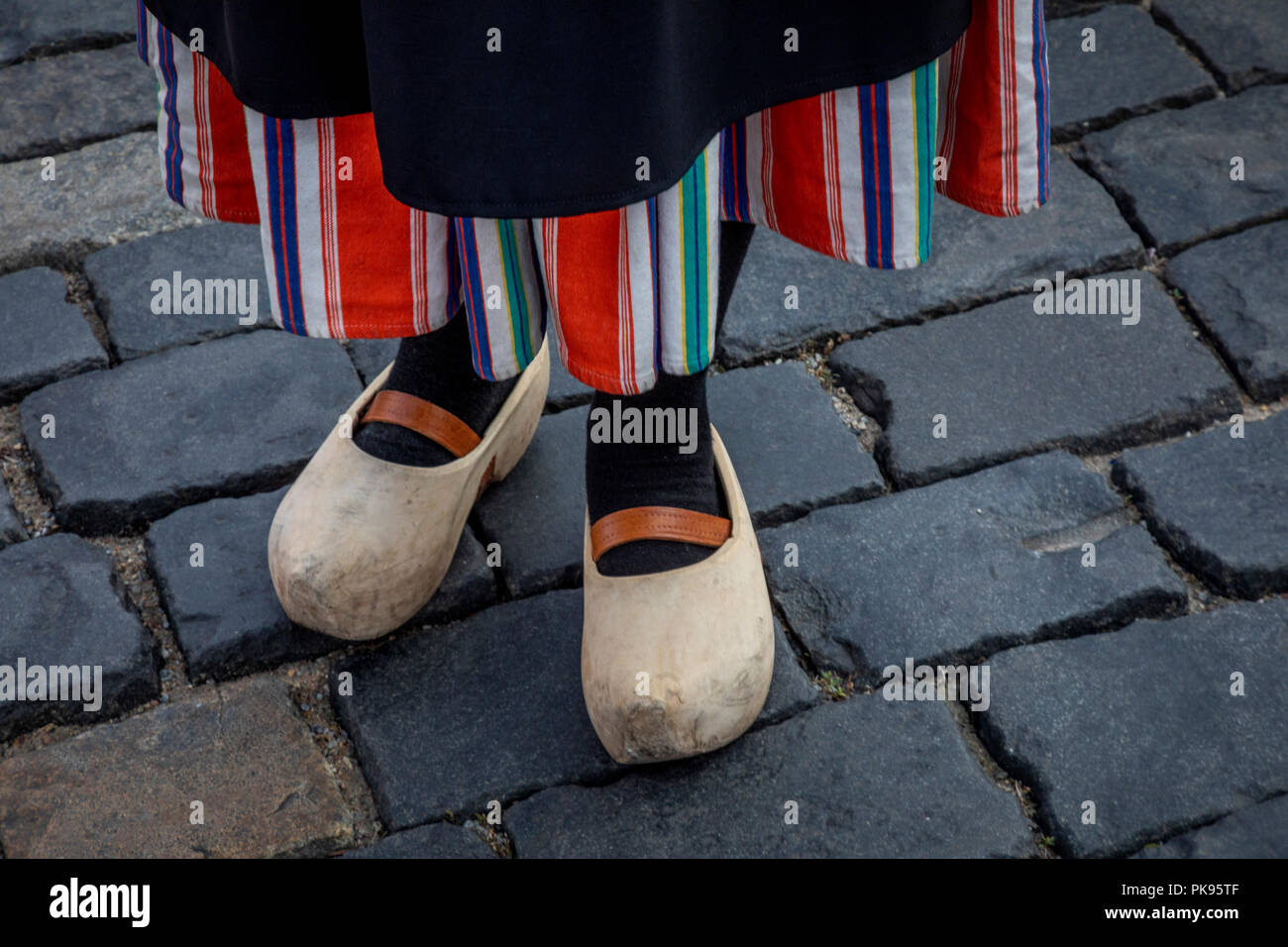 A girl with traditional Dutch clothes and wooden shoes (Klomps) stands on a cobblestone pavement Stock Photo