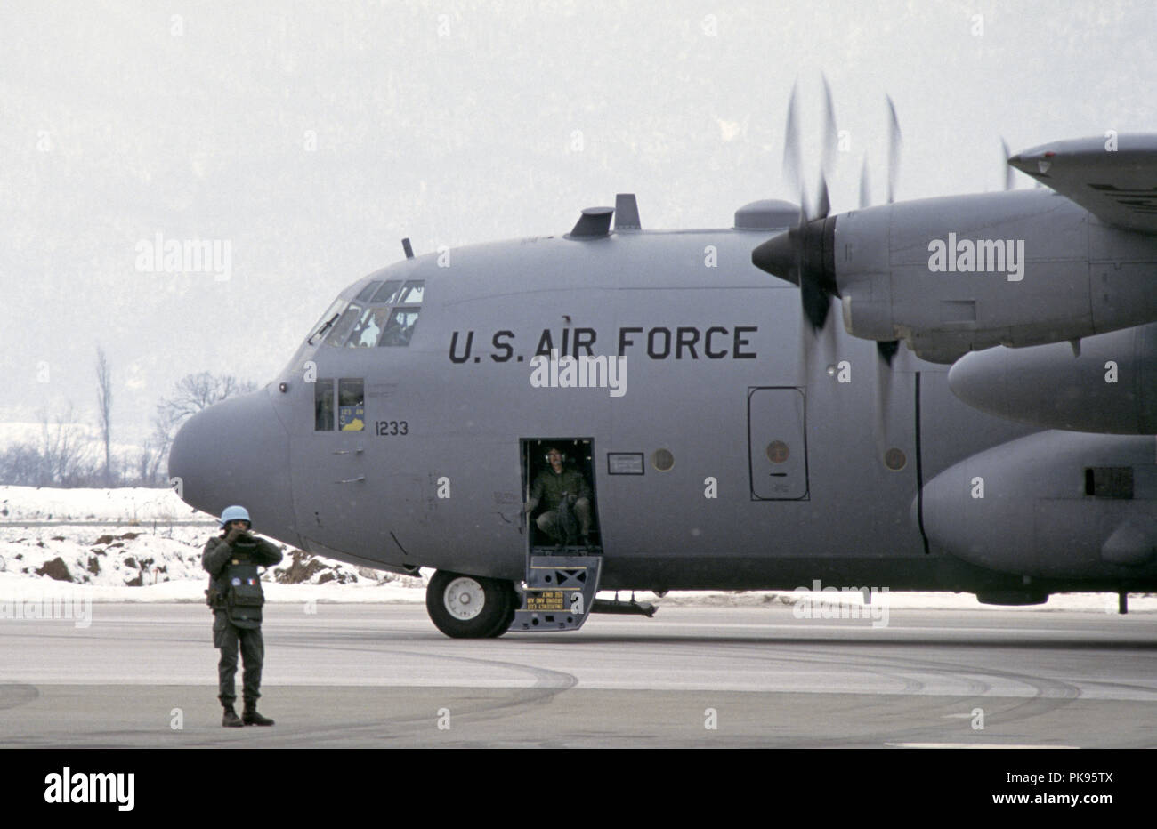 8th March 1993 During the Siege of Sarajevo: as snow falls, an American Lockheed C-130 Hercules transport jet of the Kentucky Air Guard is on the tarmac at Sarajevo Airport. A French UN soldier stands next to it, waiting to give the all clear for take-off. Stock Photo