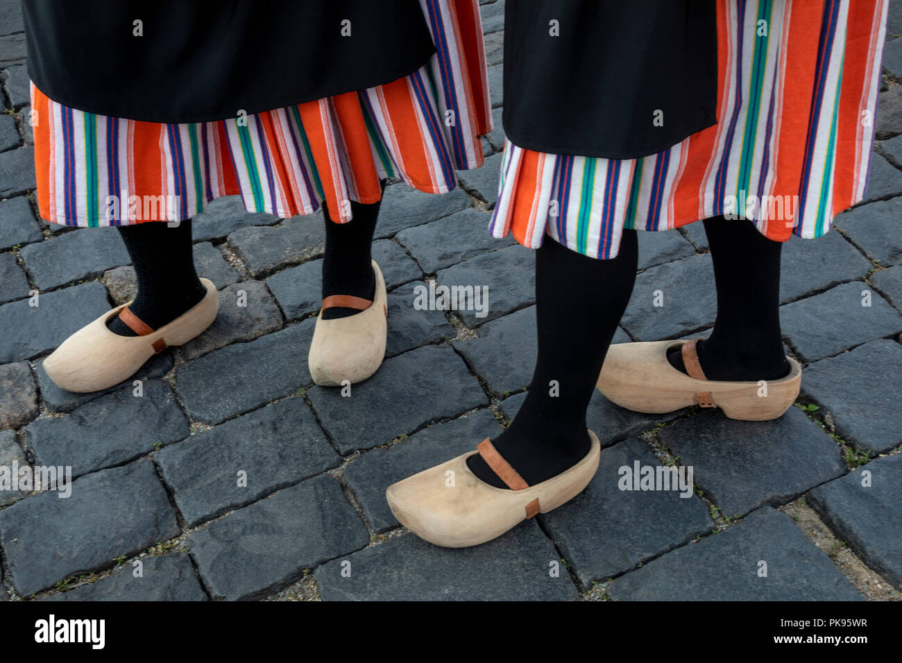 A girl with traditional Dutch clothes and wooden shoes (Klomps) stands on a cobblestone pavement Stock Photo
