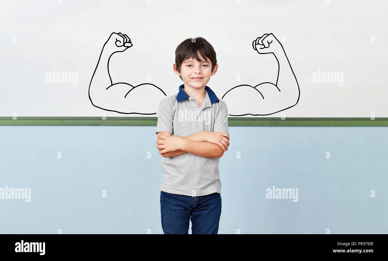 Happy schoolboy stands in elementary school in front of muscled whiteboard as a self-confidence concept Stock Photo