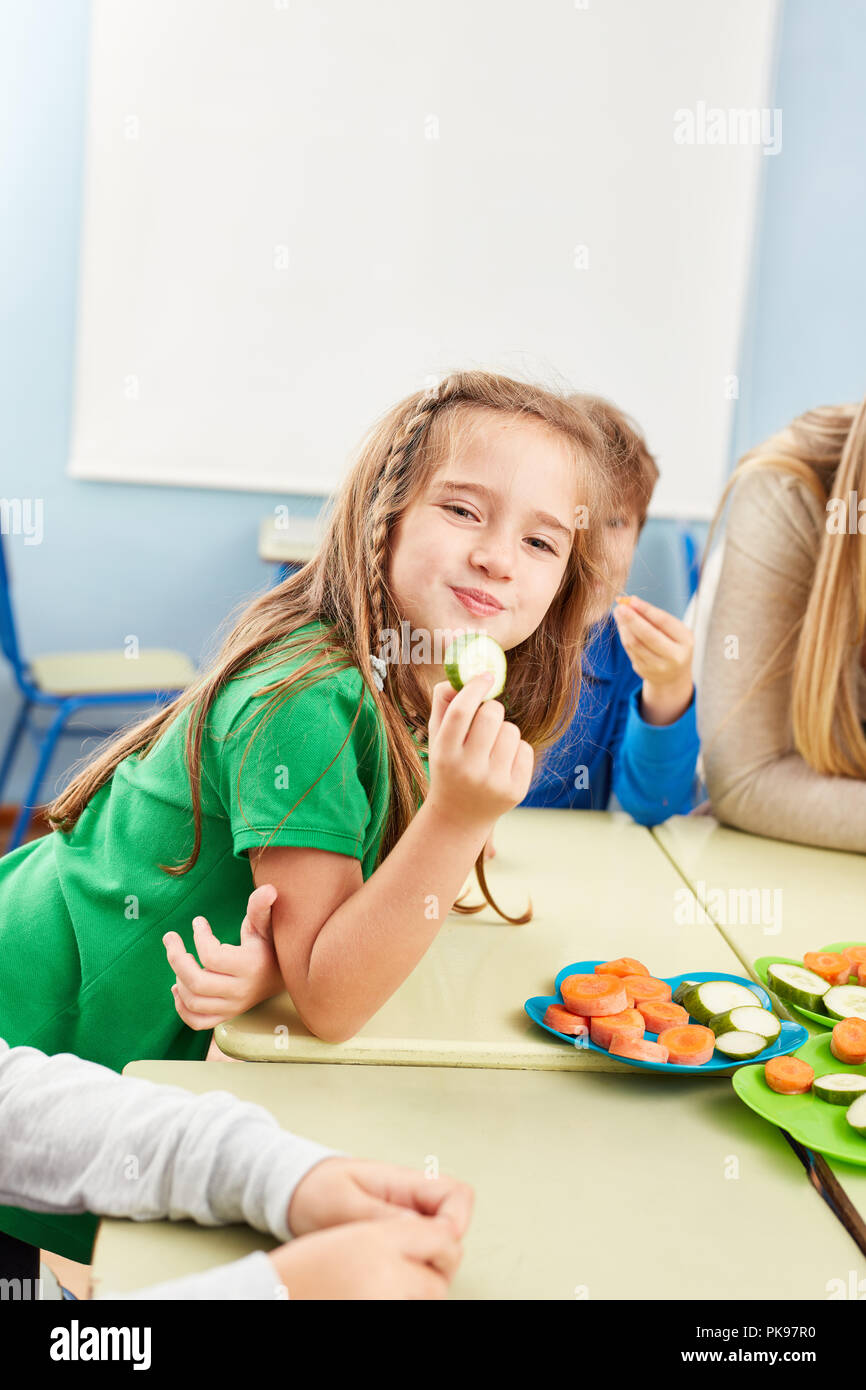 Girl is eating fresh vegetables as a snack in the cafeteria of elementary school Stock Photo