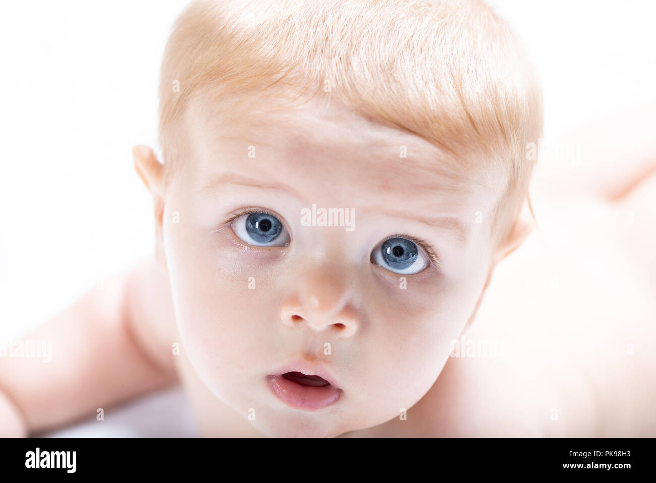 Blond baby boy with big blue eyes staring up into the camera with fascination in a high key close up cropped portrait of the face Stock Photo