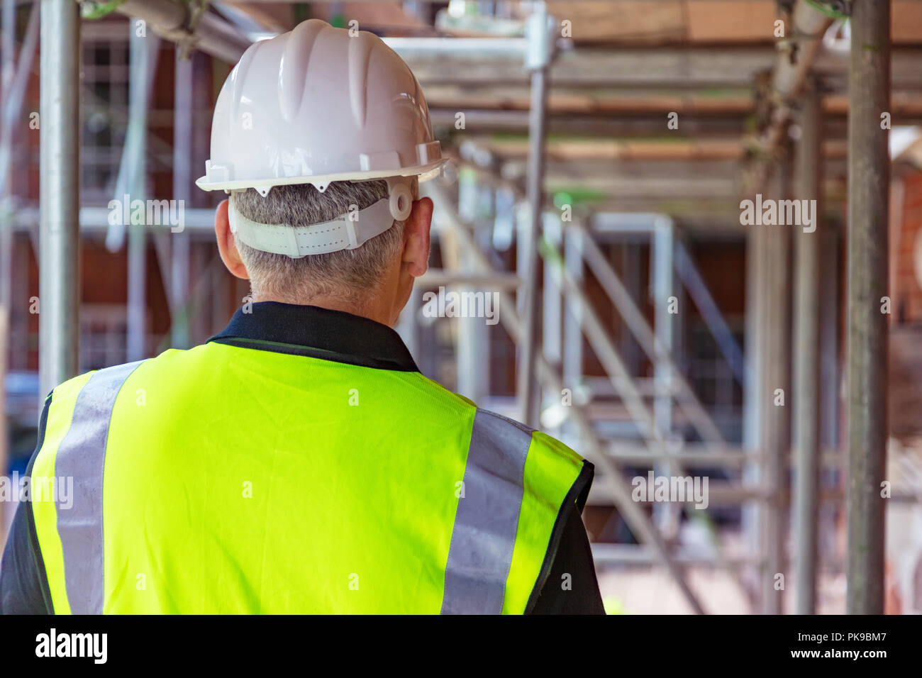 Rear view of male builder construction worker on building site wearing hard hat and hi-vis vest Stock Photo