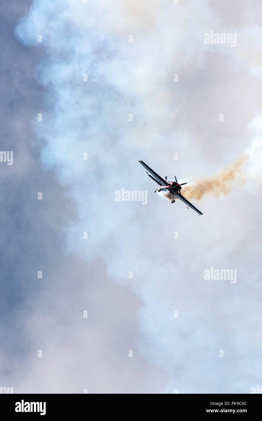 A G-Force Aerobatics Extra 300 tumbles out of an aerobatic routine trailing white smoke Stock Photo