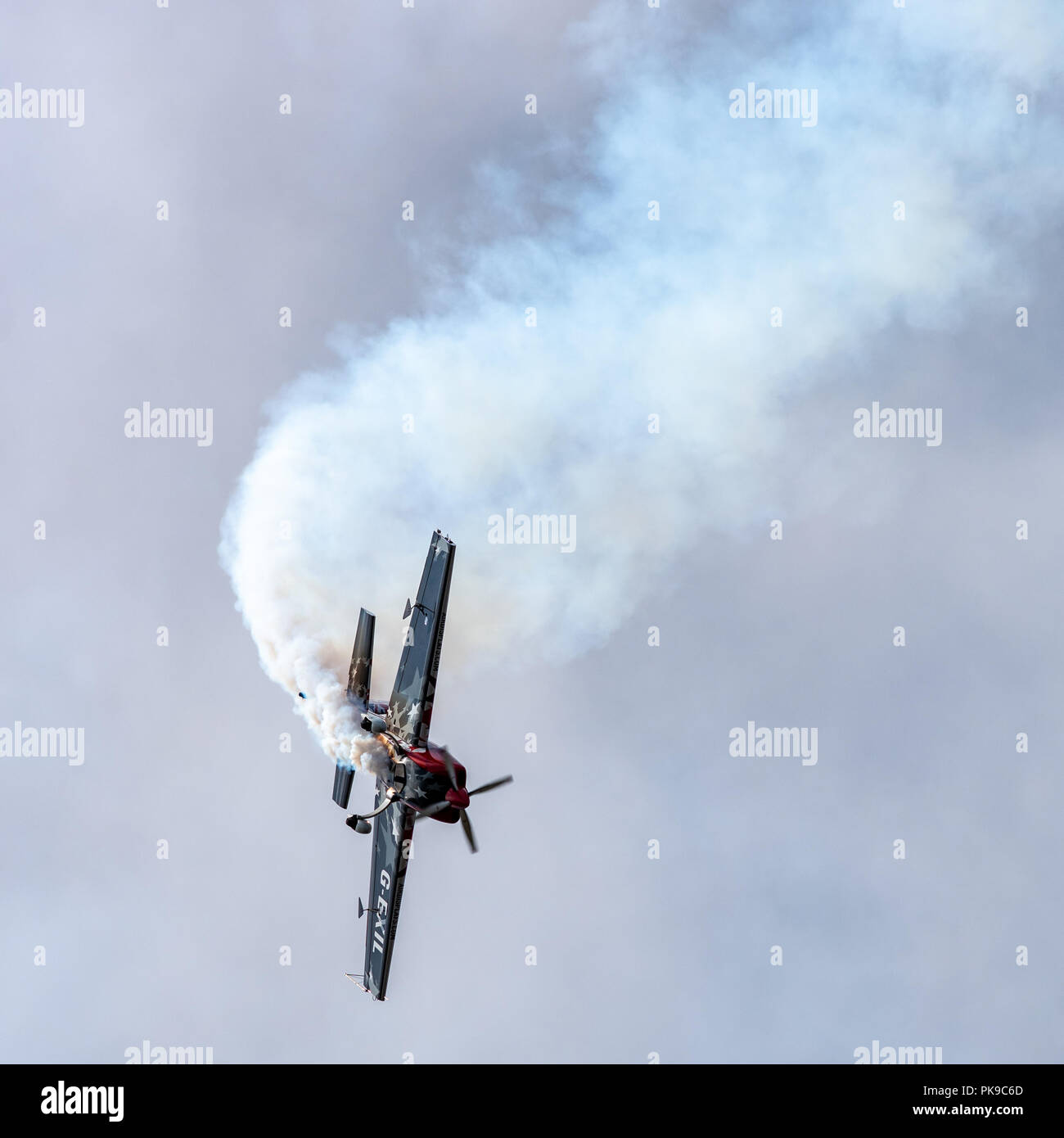 A G-Force Aerobatics Extra 300 trails a plume of white smoke as it tumbles out of a loop during an aerobatics routine Stock Photo