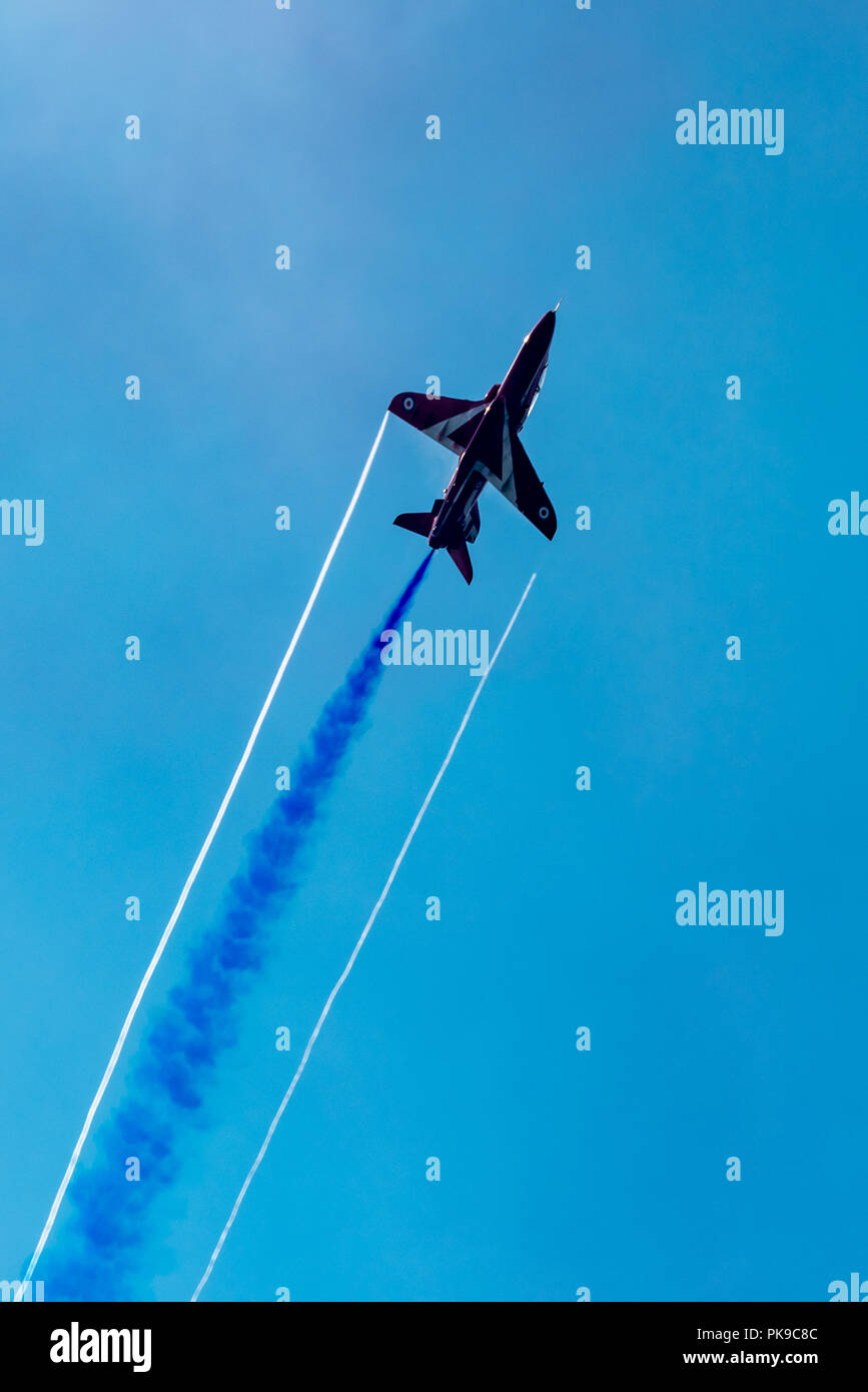 Contrasting wing tip and blue smoke trails from a BAe Hawk of the RAF's Red Arrows aerobatics display team Stock Photo