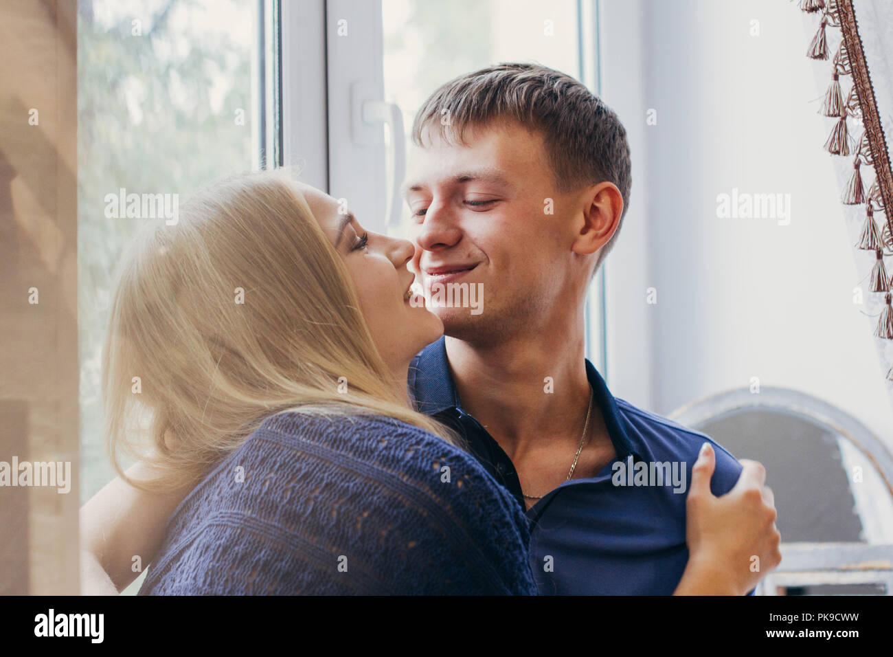 Loving couple sitting on the window, loving and gentle look. Positive emotion, smiling faces. Couple hugging and looking at each other. A man and a wo Stock Photo