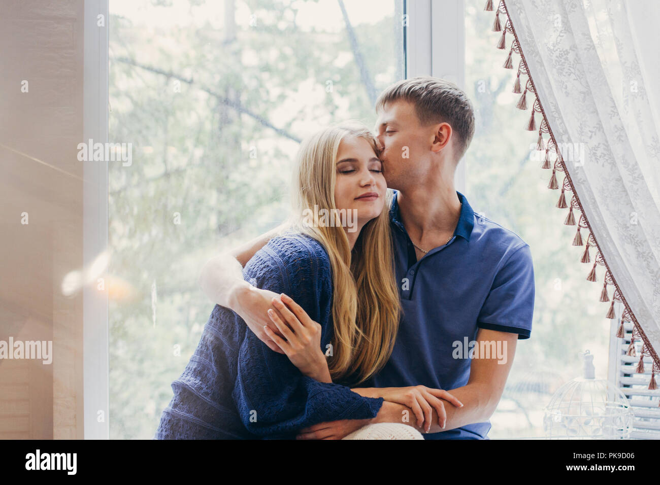 Loving couple sitting on the window, loving and gentle look. Positive emotion, smiling faces. Couple hugging and looking at each other. A man and a wo Stock Photo
