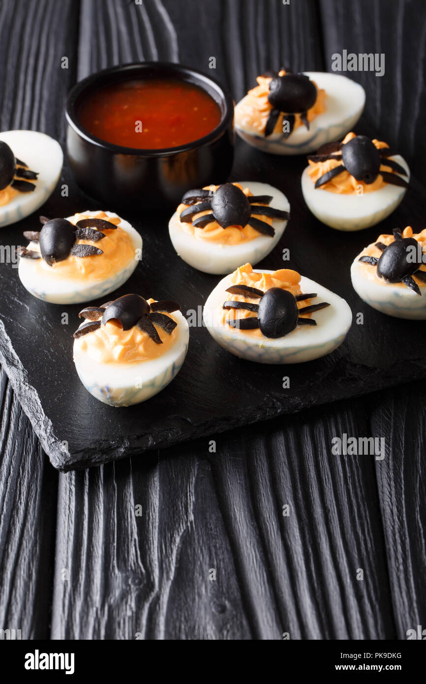 deviled eggs stuffed with mustard and yolk decorated with olive spiders close-up served with ketchup on a black table. vertical Stock Photo