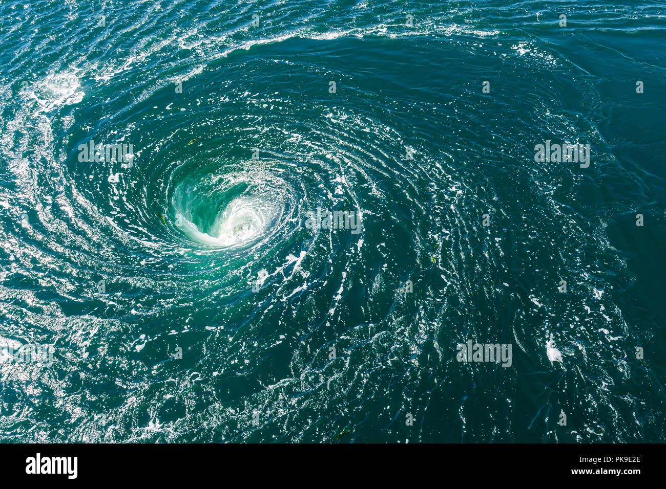 High angle view of a powerful whirlpool at the surface of green water with foam. Stock Photo