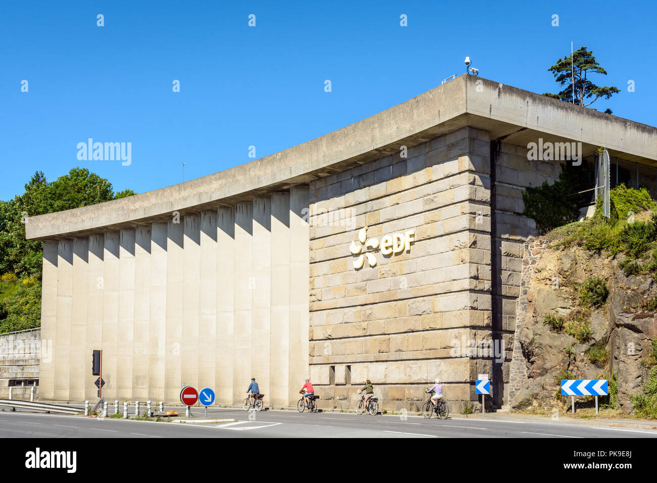 A building of the Rance tidal power station run by french public electricity utility company EDF near Saint-Malo in Brittany with cyclists passing by. Stock Photo