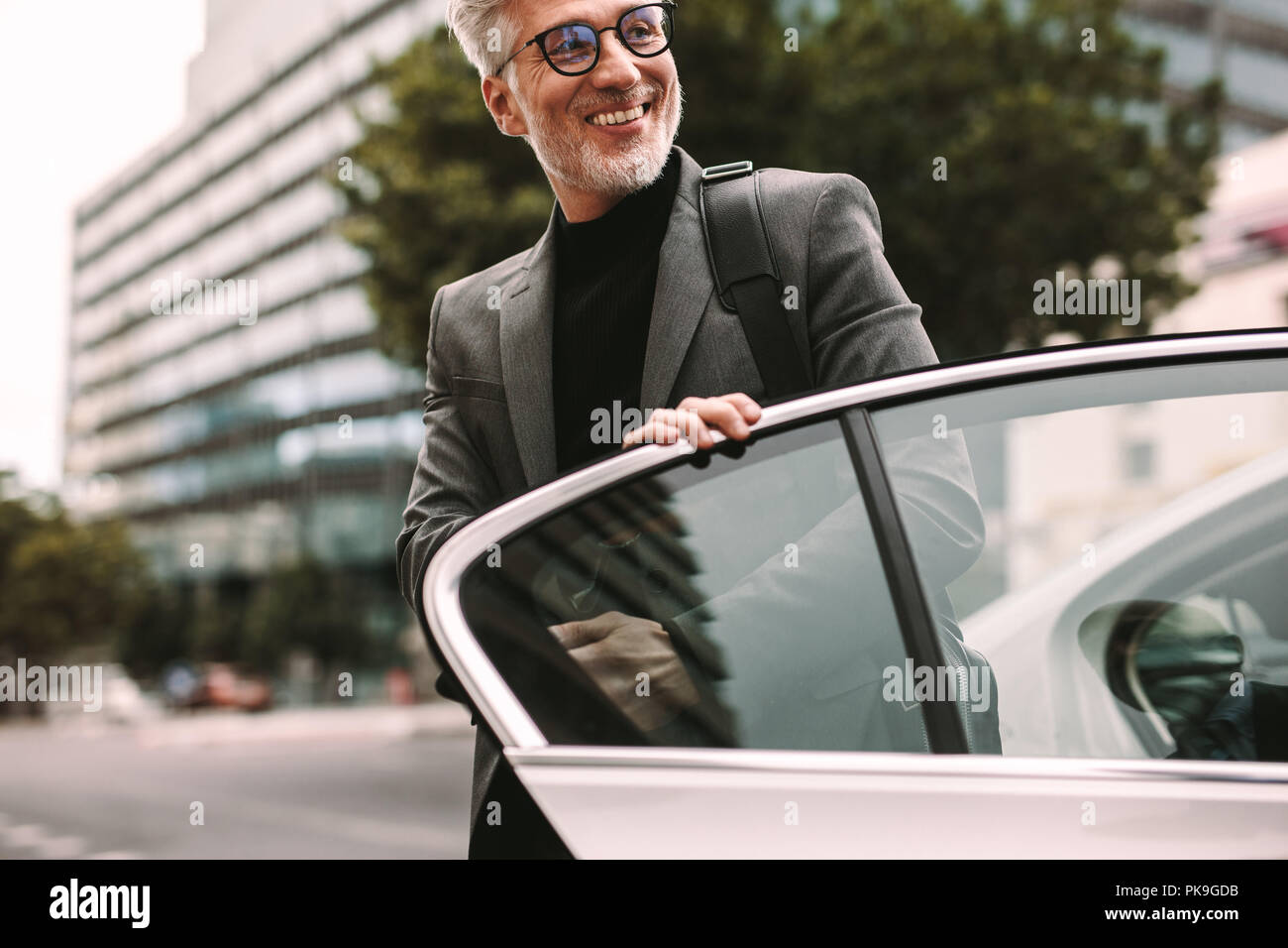 Happy mature commuter getting out of a taxi. Businessman getting off a cab. Stock Photo