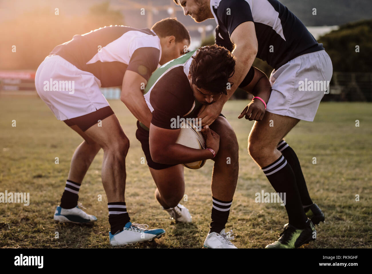 Professional rugby player is blocked by the opposite team player on ground. Rugby players striving to get to the ball during the match. Stock Photo