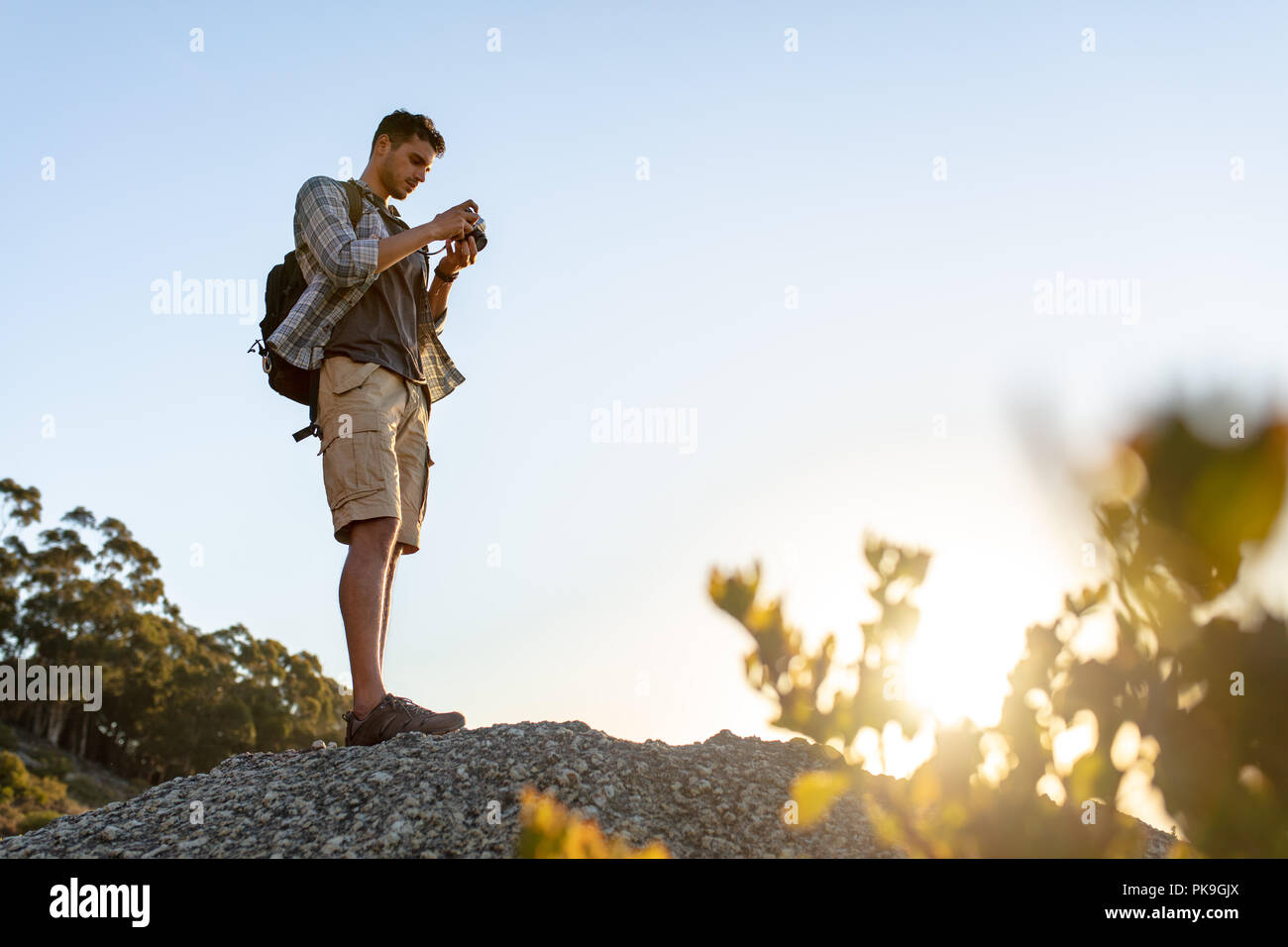 Man standing on the top of hill with digital camera and checking the pictures. Male hiker photographing a landscape view from mountain top. Stock Photo