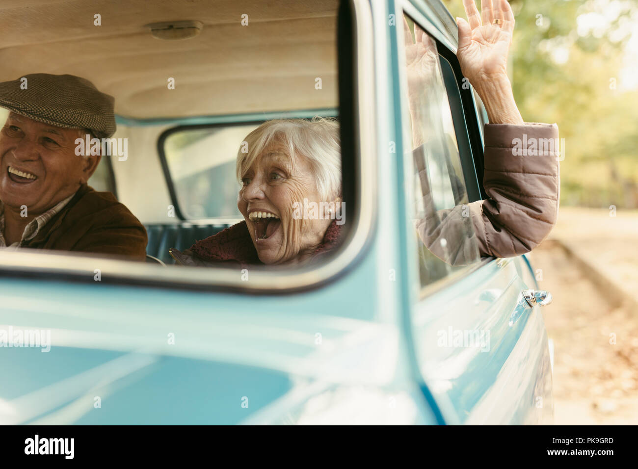 Senior woman enjoying road trip with her husband. Excited old female raising her hand out of the car and laughing. Senior couple enjoying on their roa Stock Photo