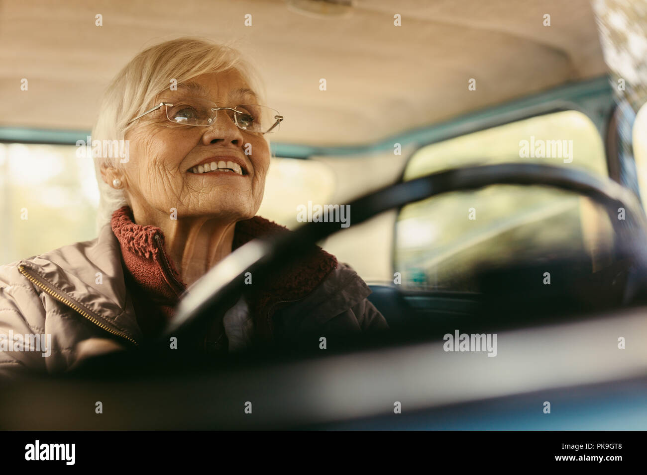 Senior woman driving car on winter day concentrating on the road. Elderly female wearing glasses driving a car carefully. Stock Photo