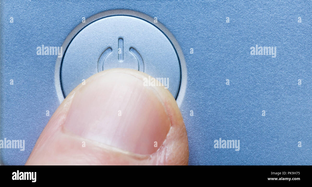 Close up of person's finger pressing computer electronic device on/off power button. Modern technology symbol icon. Stock Photo