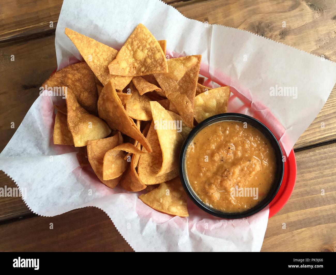 Overhead flat lay view of traditional casual Mexican snack foods tortilla chips and salsa in plastic basket lined with paper on rustic wooden table Stock Photo