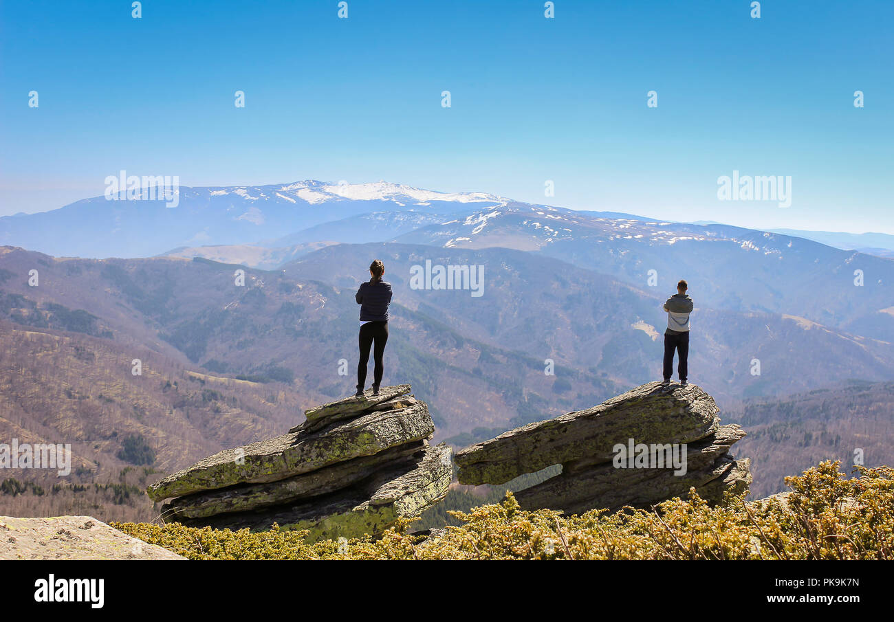 Young couple standing on two large rocks at the mountain summit and ...