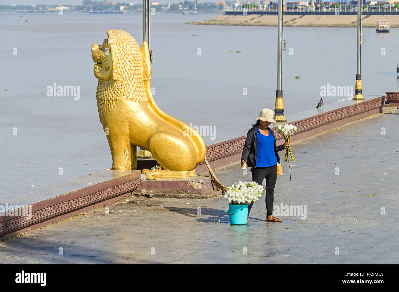 Phnom Penh, Cambodia - April 9, 2018: Preah Sisowath Quay along the banks of the Mekong and Tonle Sap with a lion statue and a woman selling lotus Stock Photo