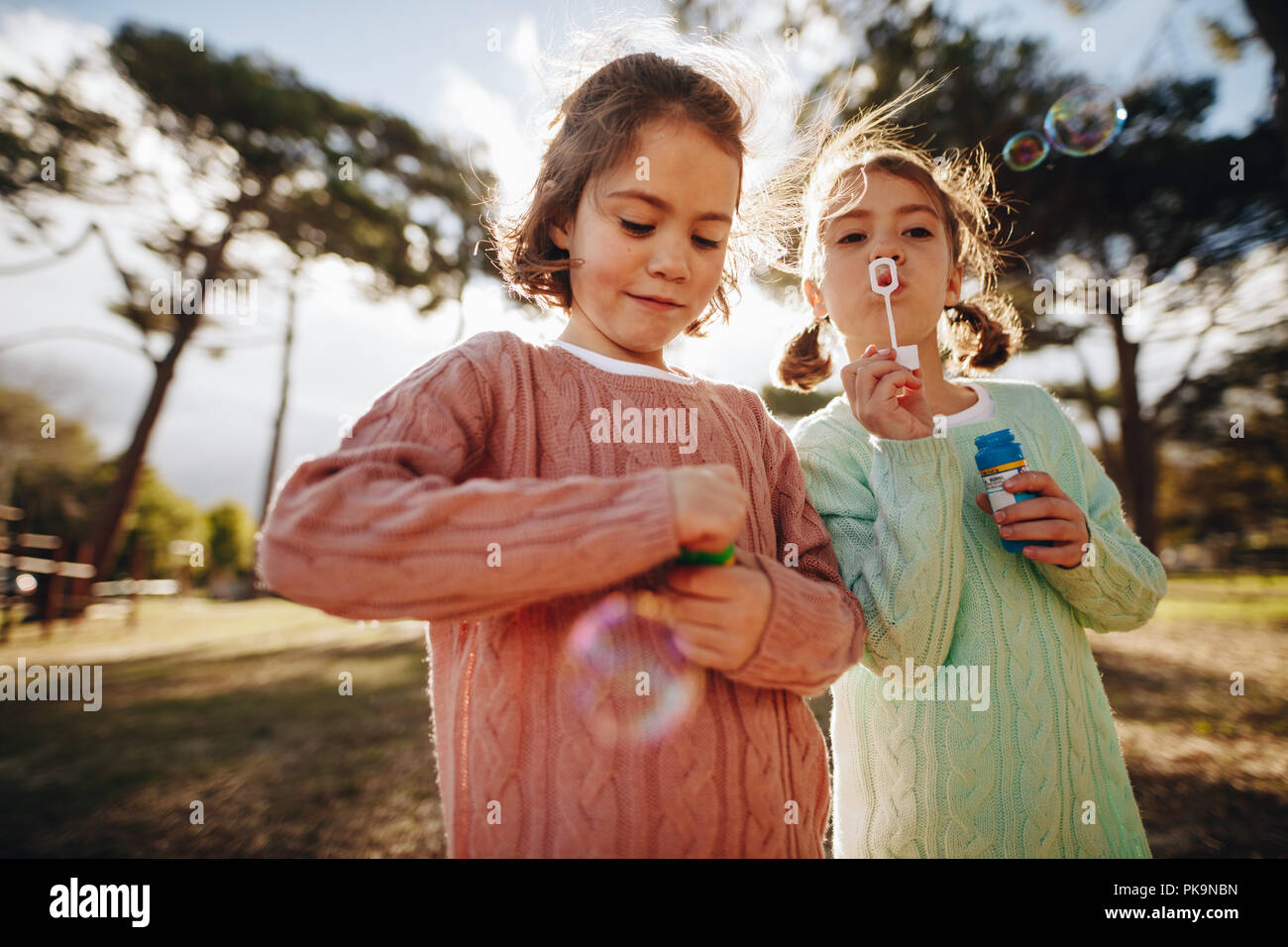 Beautiful little girls playing with bubbles at the playground. Cute twin sisters blowing soap bubbles outdoors. Stock Photo