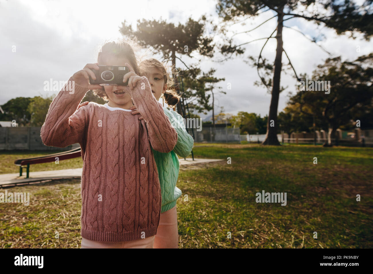 Two little girls playing at the park with old camera. Twin sisters taking pictures with old camera at the playground. Stock Photo