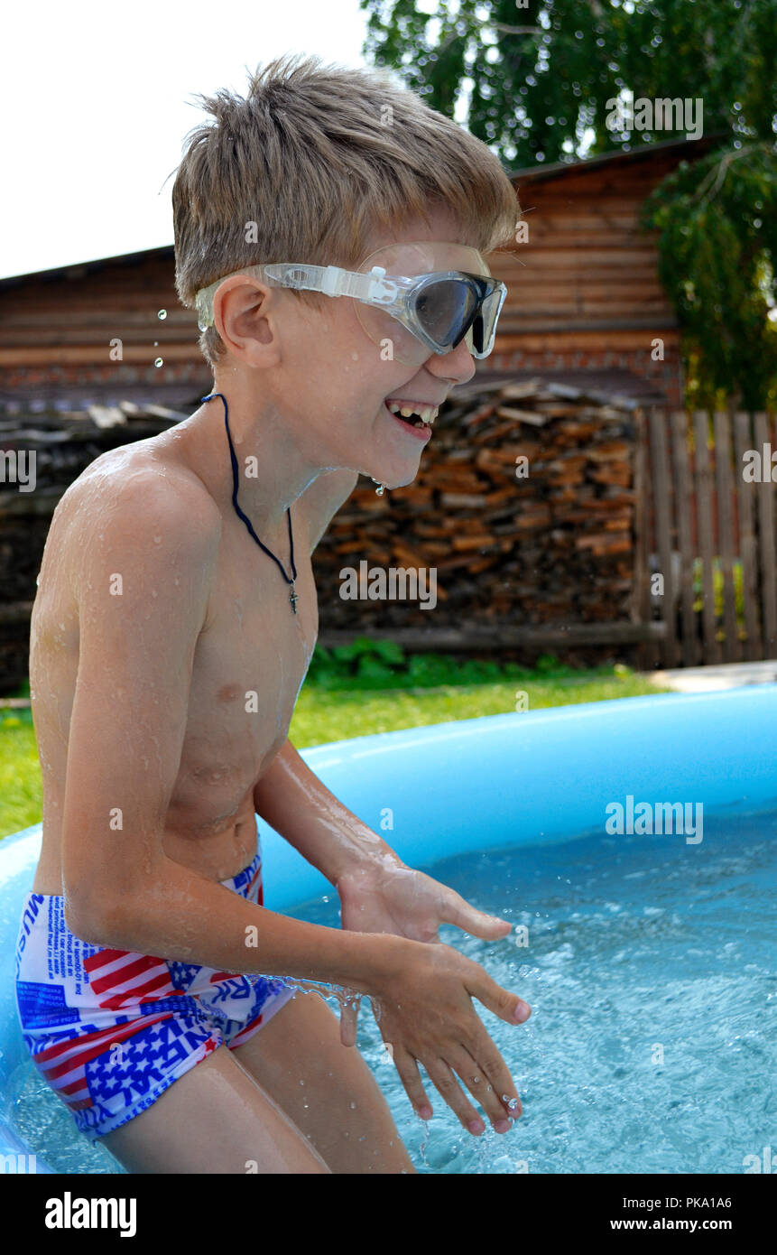 A boy-schoolboy is bathed in the summer during a vacation in a home inflatable pool with clear blue water in the yard of the house Stock Photo