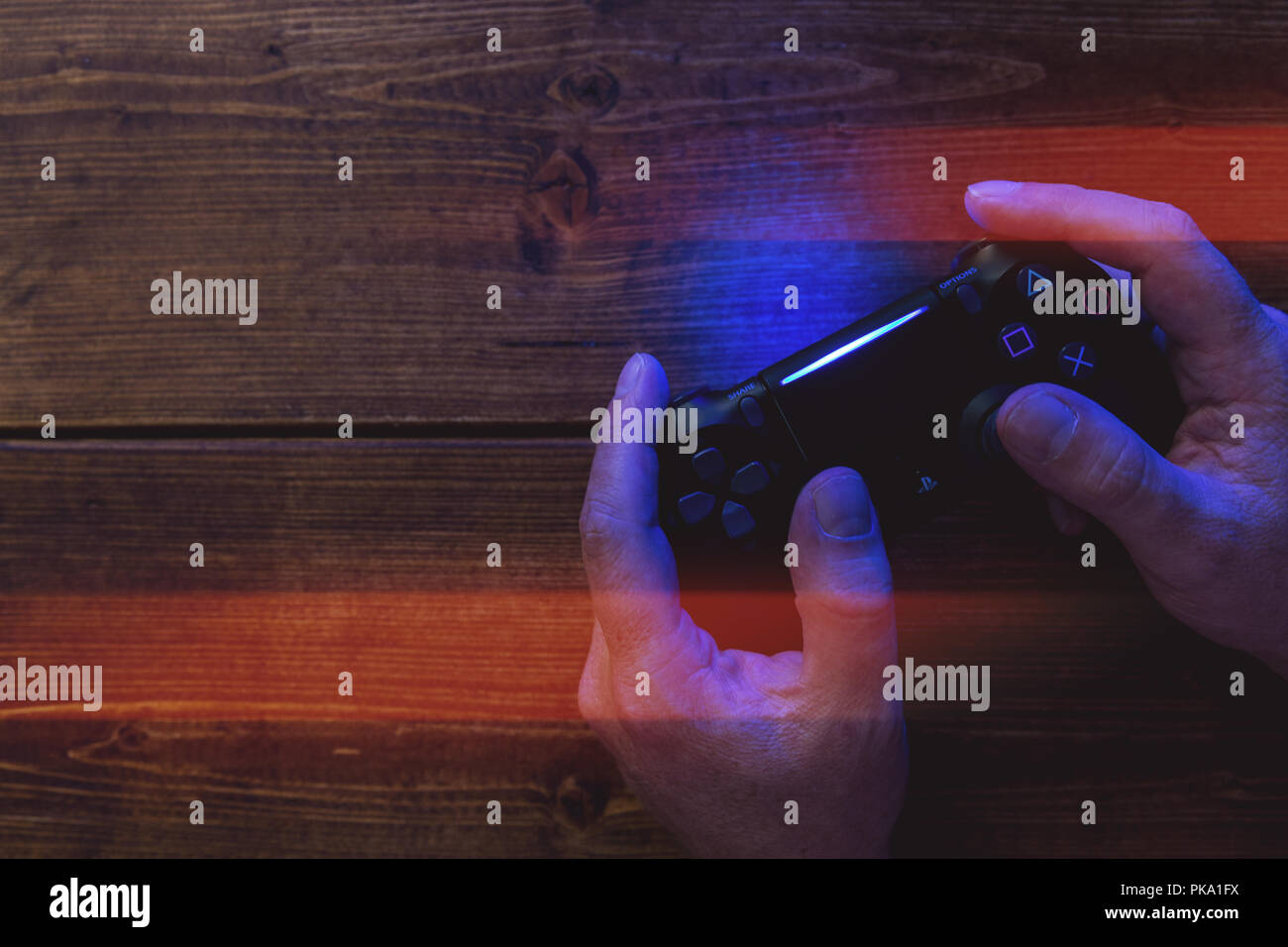 Man playing video games PlayStation gaming controller on wood background with lights Stock Photo