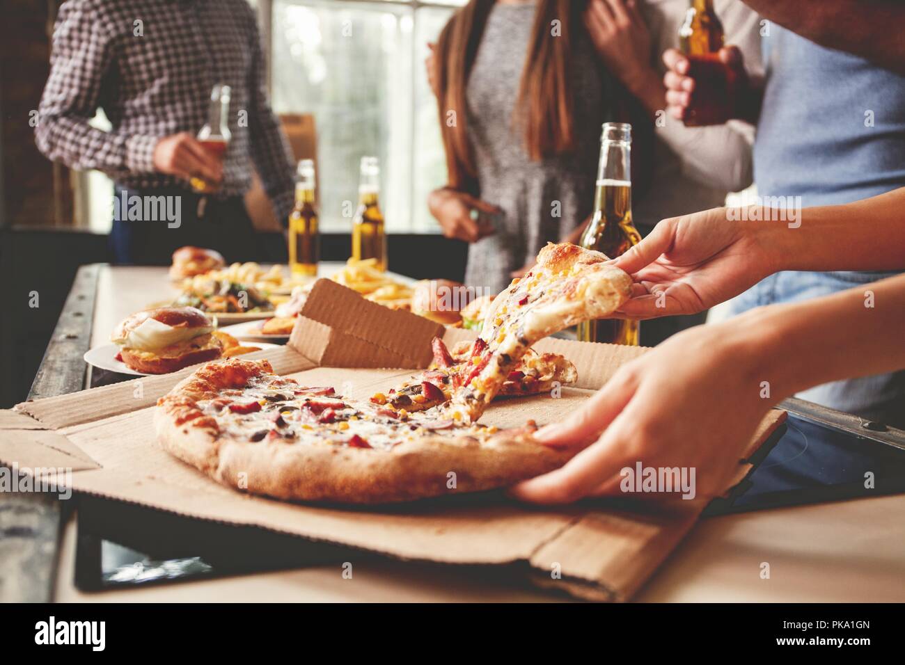 Friends taking slices of tasty pizza from plate, close up view. Stock Photo