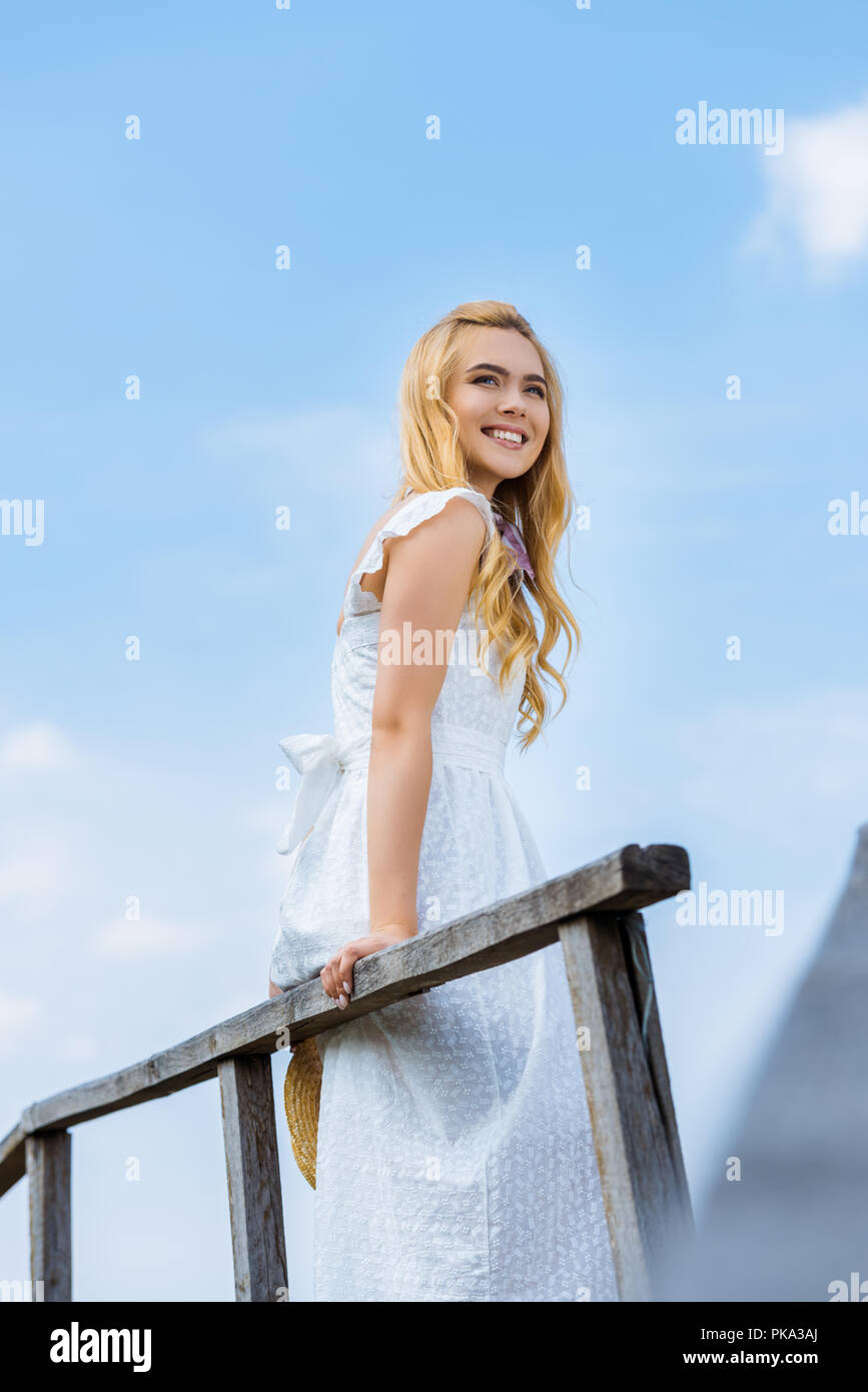low angle view of happy blonde girl smiling and looking away against blue sky Stock Photo