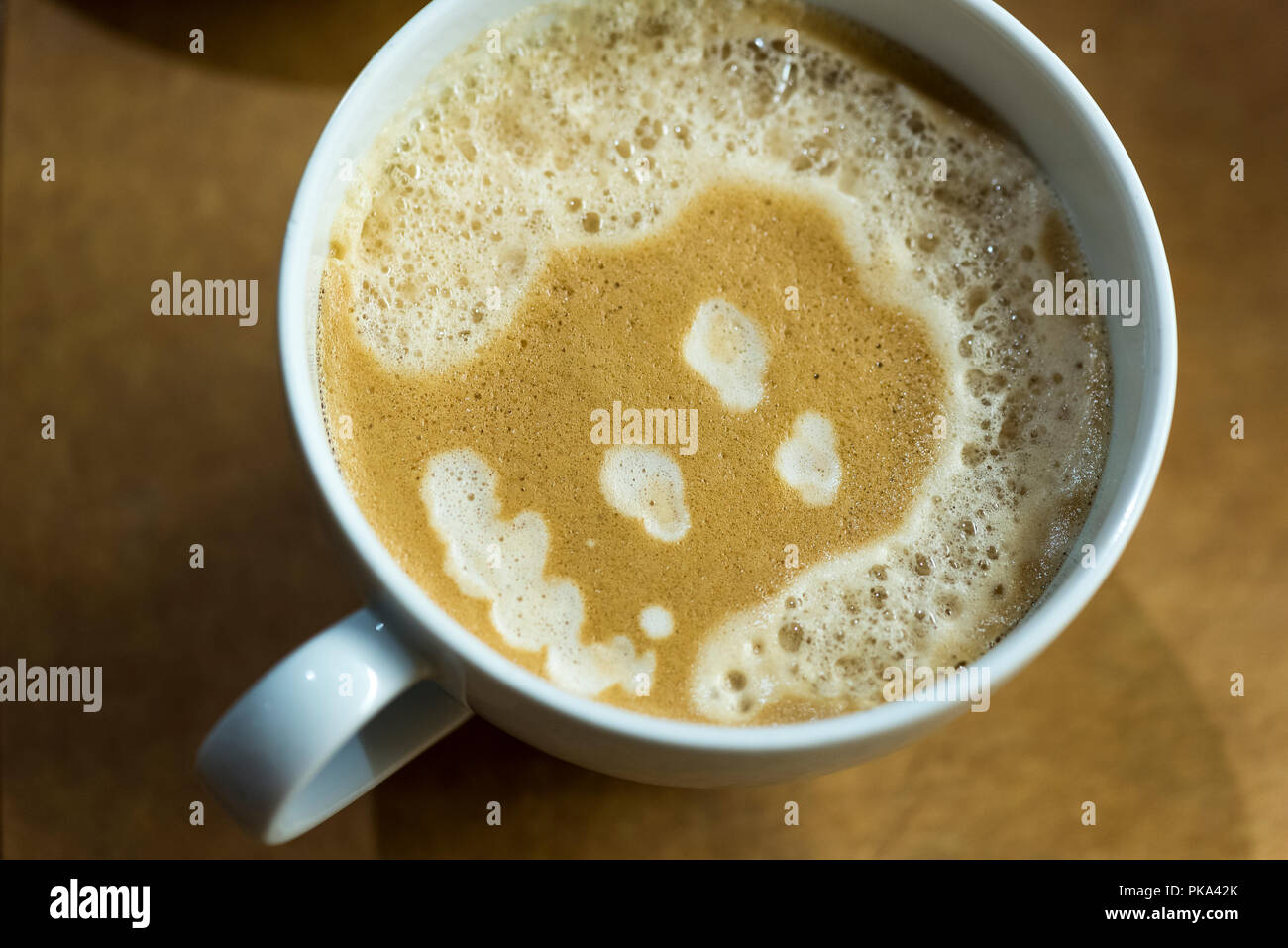 A face with curly hair is formed by the bubbles in the foam of a latte. Stock Photo