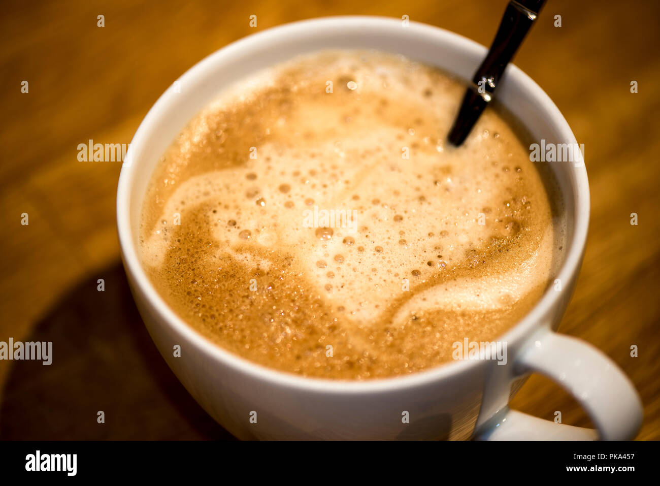 Bubbles form in the foam of a latte in a white cup. Stock Photo