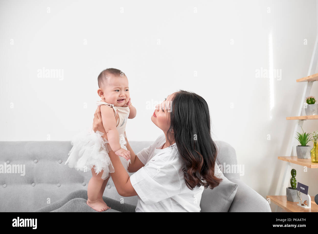 Mother and baby laugh together at home. They are sitting on the sofe in a brightly lit living room at the weekend together, lazy morning, warm and coz Stock Photo