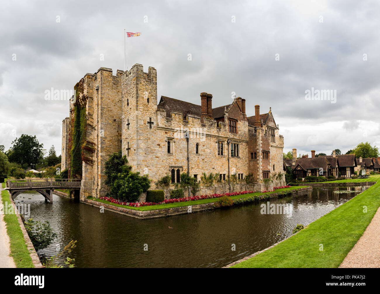 HEVER CASTLE, ENGLAND, UK – SEPTEMBER 08 2018: View of Hever Castle and its moat on a cloudy day, with a flag flying at full mast. Stock Photo
