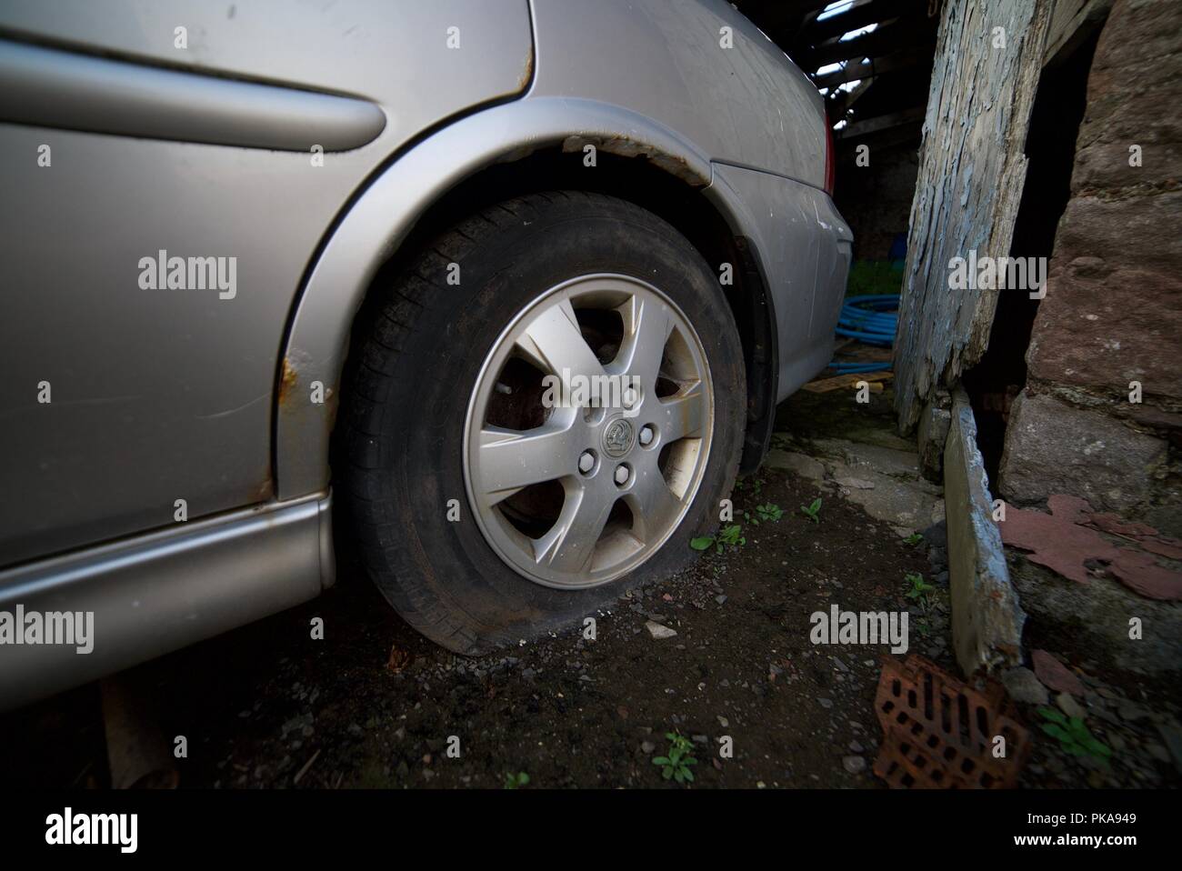 Popped tyre on a car (grey vauxhall with deflated back tyre from puncture) Stock Photo