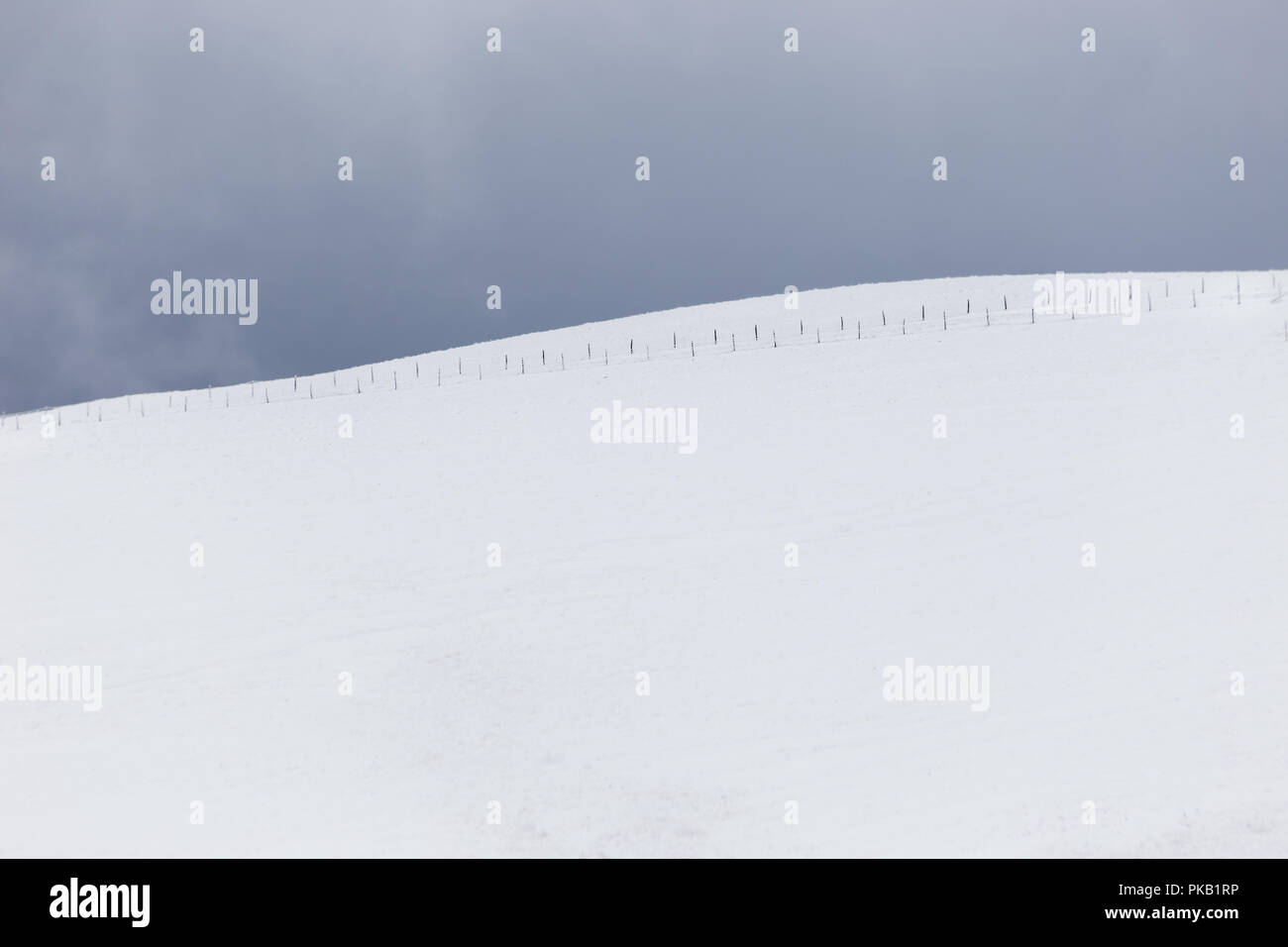 A very minimalistic view of a mountain covered by snow, with a fence Stock Photo