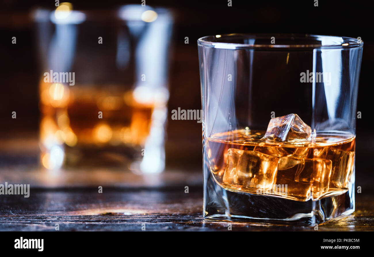 Alcohol drink whisky, whiskey or bourbon with ice cubes on dark wood