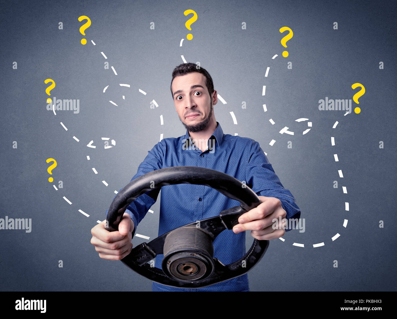 Young man holding black steering wheel with question marks around him