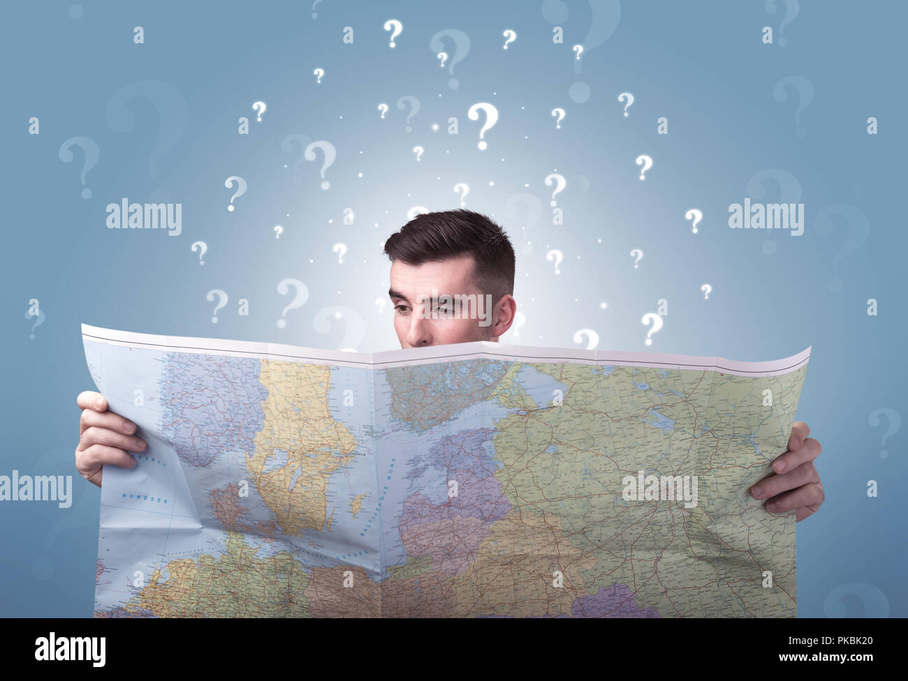 Handsome young man holding a map with white question marks above his ...