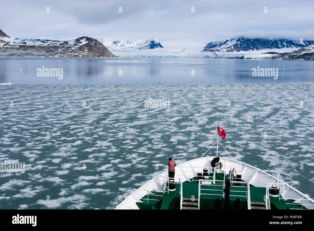 G Adventures Expedition cruise ship bow sailing through thin sea ice towards a glacier in a fjord in summer. Spitsbergen Svalbard Archipelago Norway Stock Photo