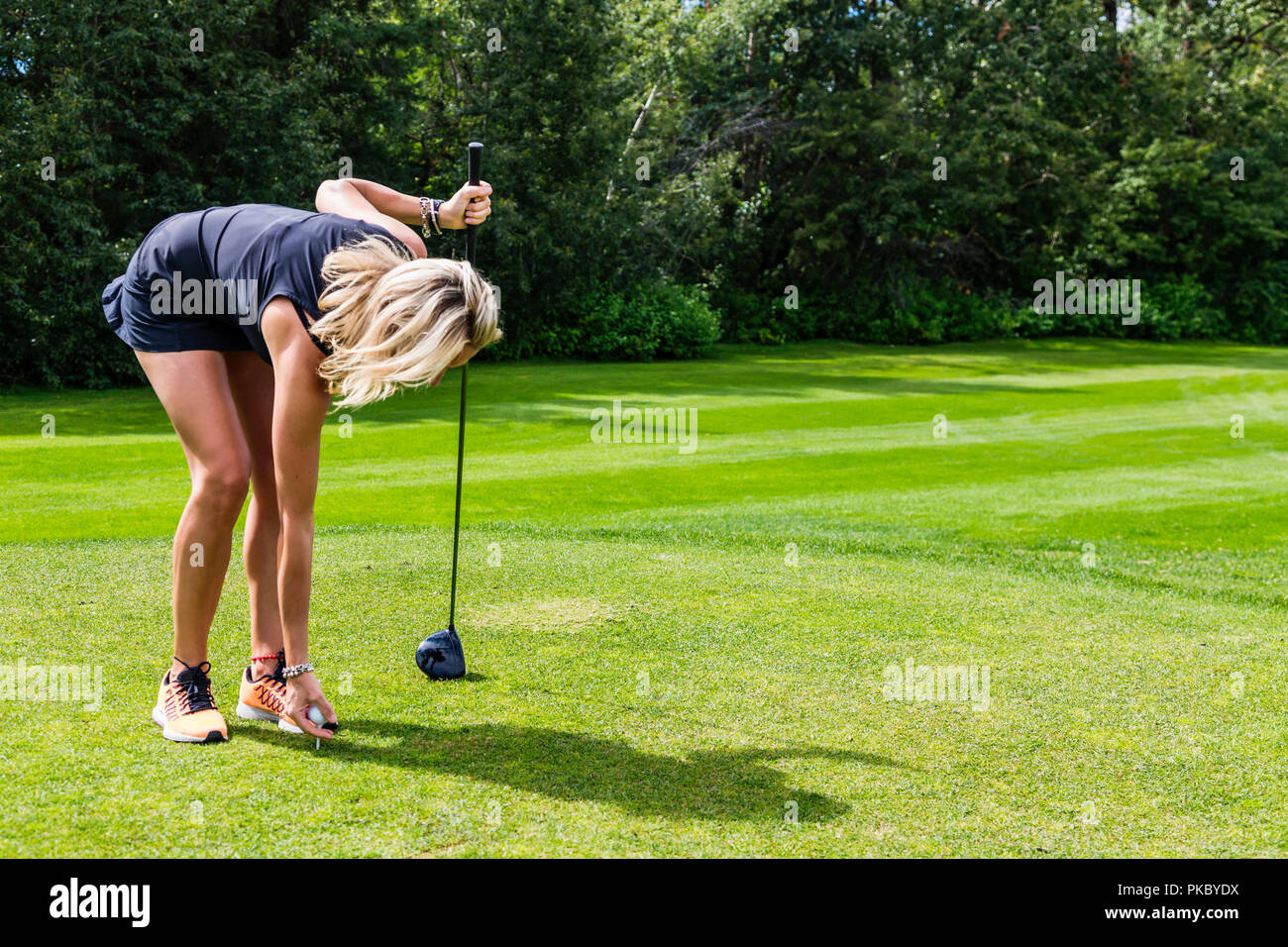 A female golfer places a golf ball on a tee while holding her driver