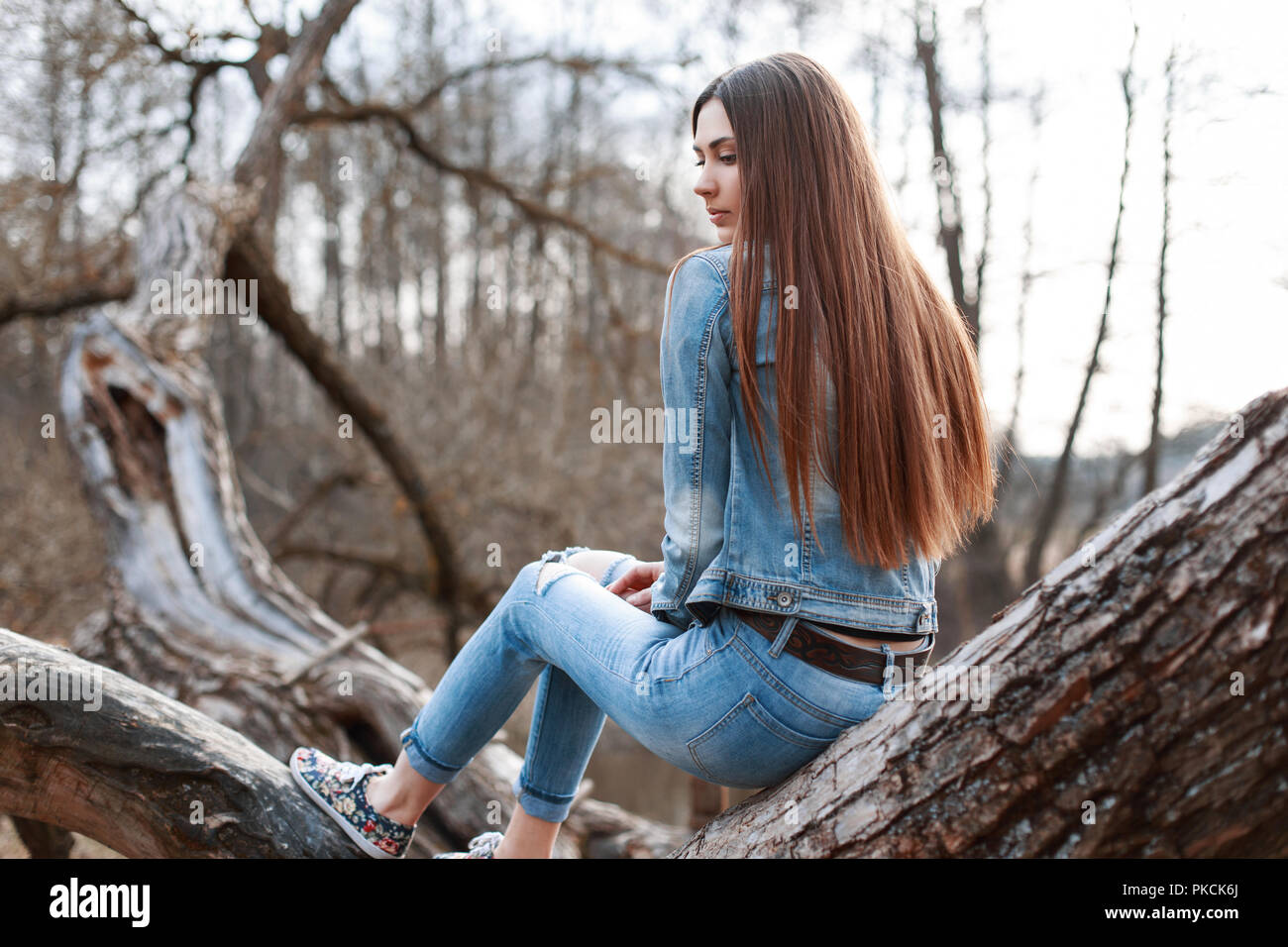 Young beautiful girl in denim jacket and jeans sits on a tree and dreams  Stock Photo - Alamy