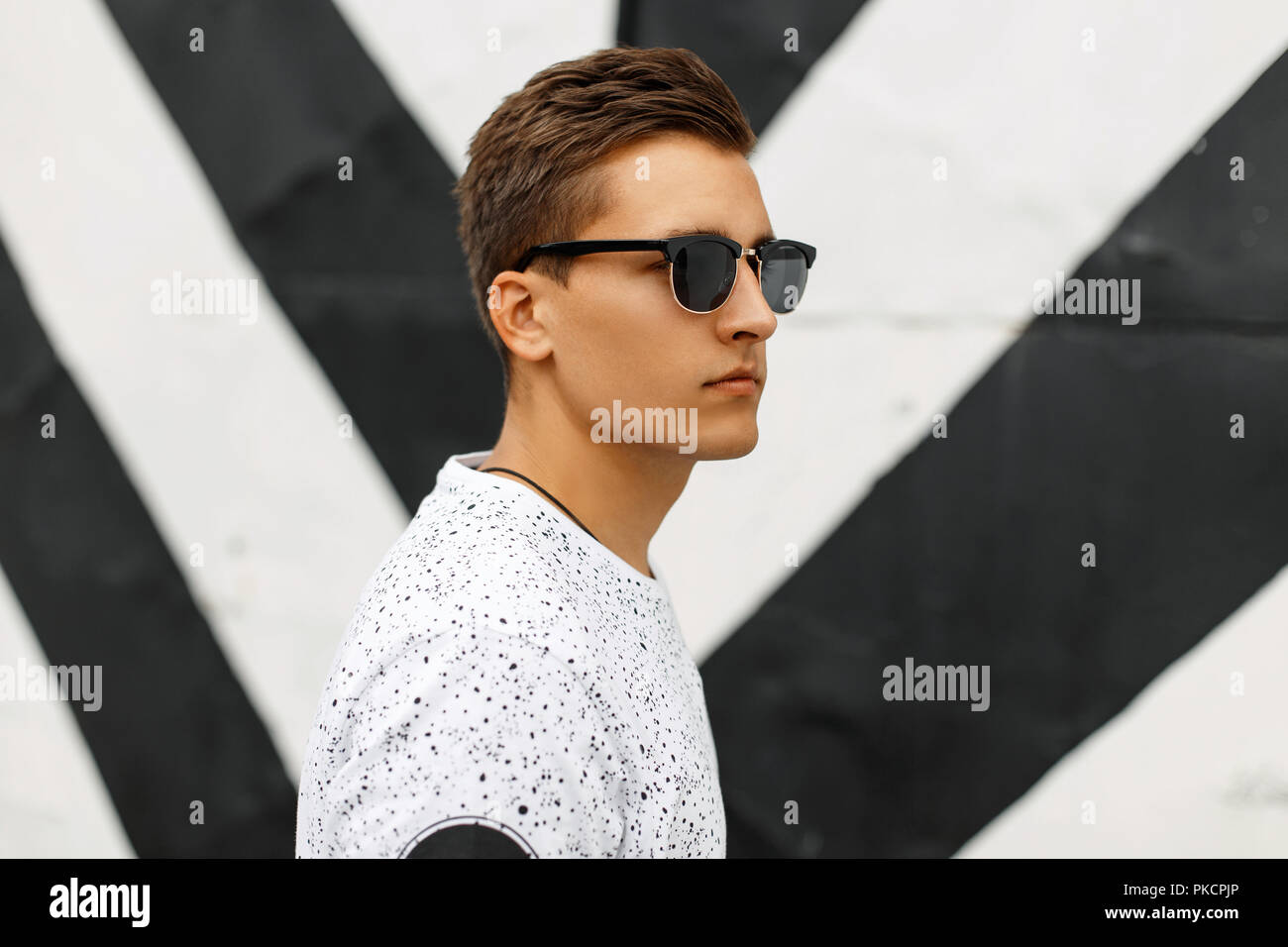 Young handsome guy with a hairstyle and sunglasses on a background of black and white stripes. Stock Photo