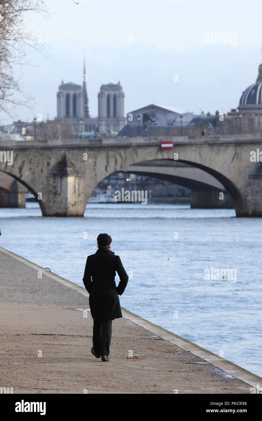 French woman walking alone along the banks of the Seine river in Paris Stock Photo